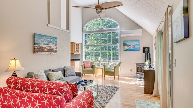 A spacious living room with a high ceiling, a large window, and a ceiling fan. - 1/2 Mi to Ogunquit Beach: Maine Home w/ Deck! (Ogunquit)
