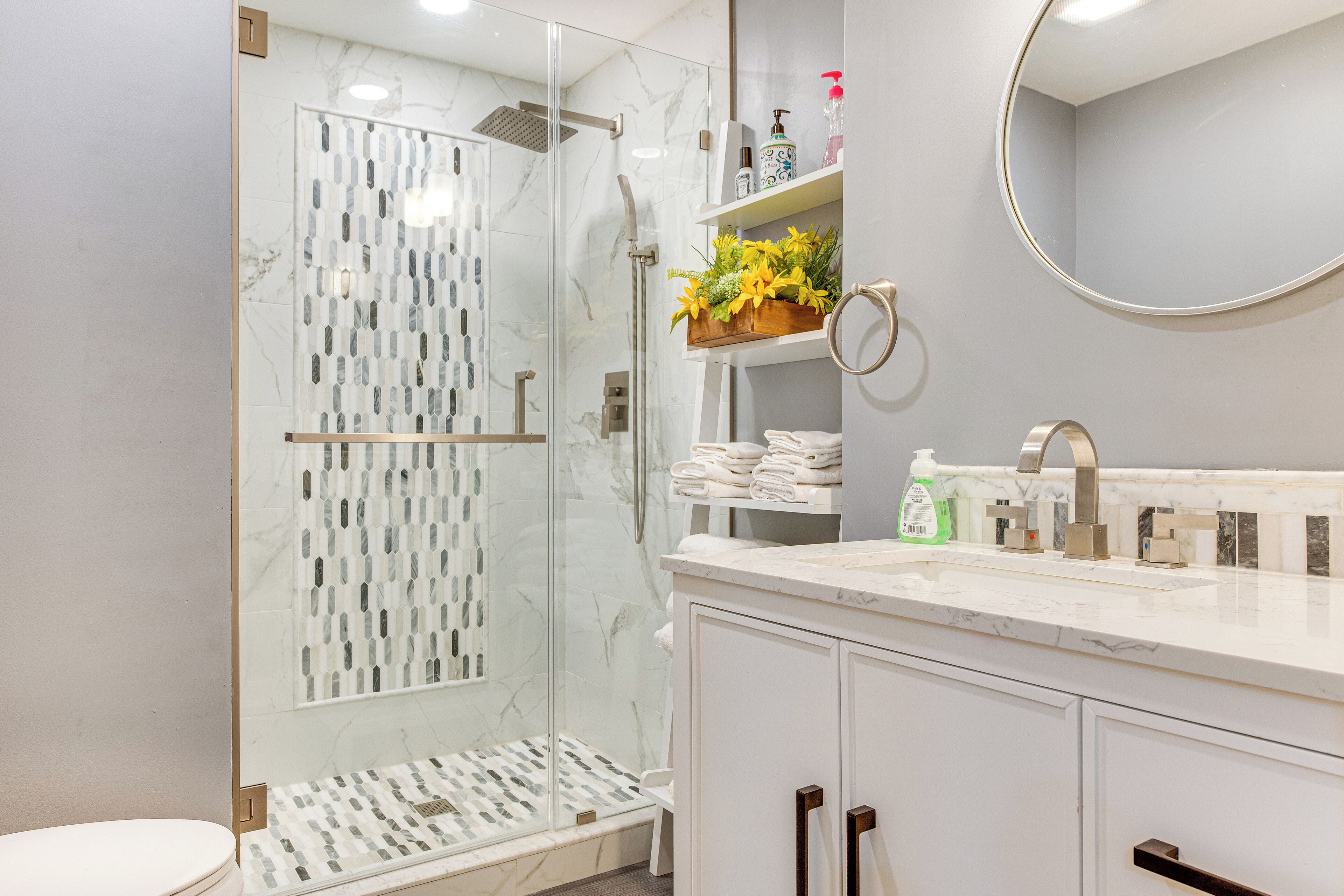 A modern bathroom with a glass-enclosed shower, marble flooring, white cabinetry, and a built-in sink with a mirror above.