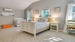 A bedroom with a sloped ceiling, a crib, a bed with a headboard, a nightstand, and a window with curtains. - 1/2 Mi to Ogunquit Beach: Maine Home w/ Deck! (Ogunquit)