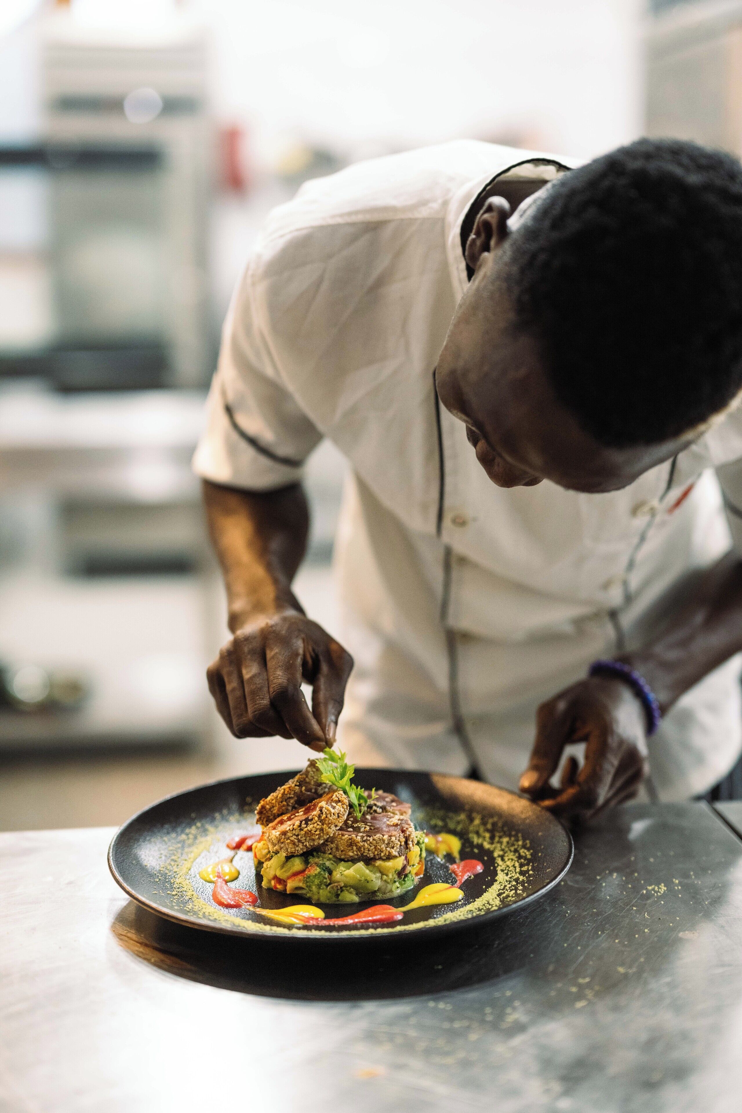 Um chef montando um prato com uma variedade de ingredientes coloridos em um prato preto.