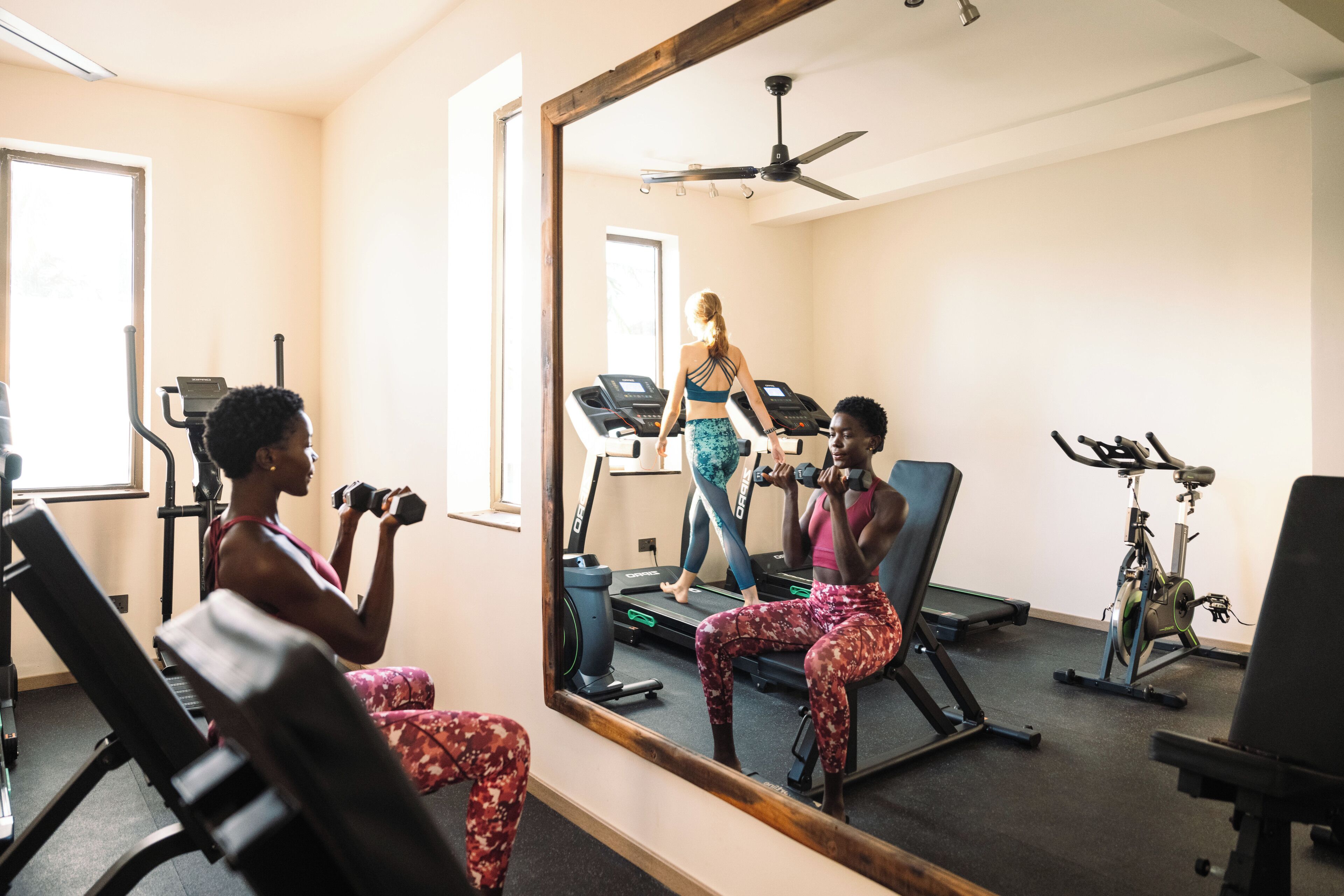 A gym with exercise equipment, a treadmill, and a mirror reflecting the room.