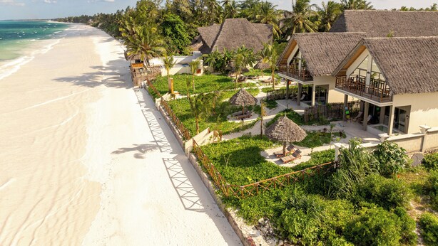 Ein Strandresort mit Villen mit Strohdächern, einem Sandstrand und üppiger Vegetation.