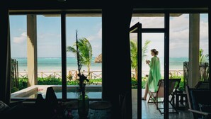 Ein Zimmer mit großen Fenstern und Meerblick, ein kleiner Tisch mit einer Vase sowie ein Stuhl.
