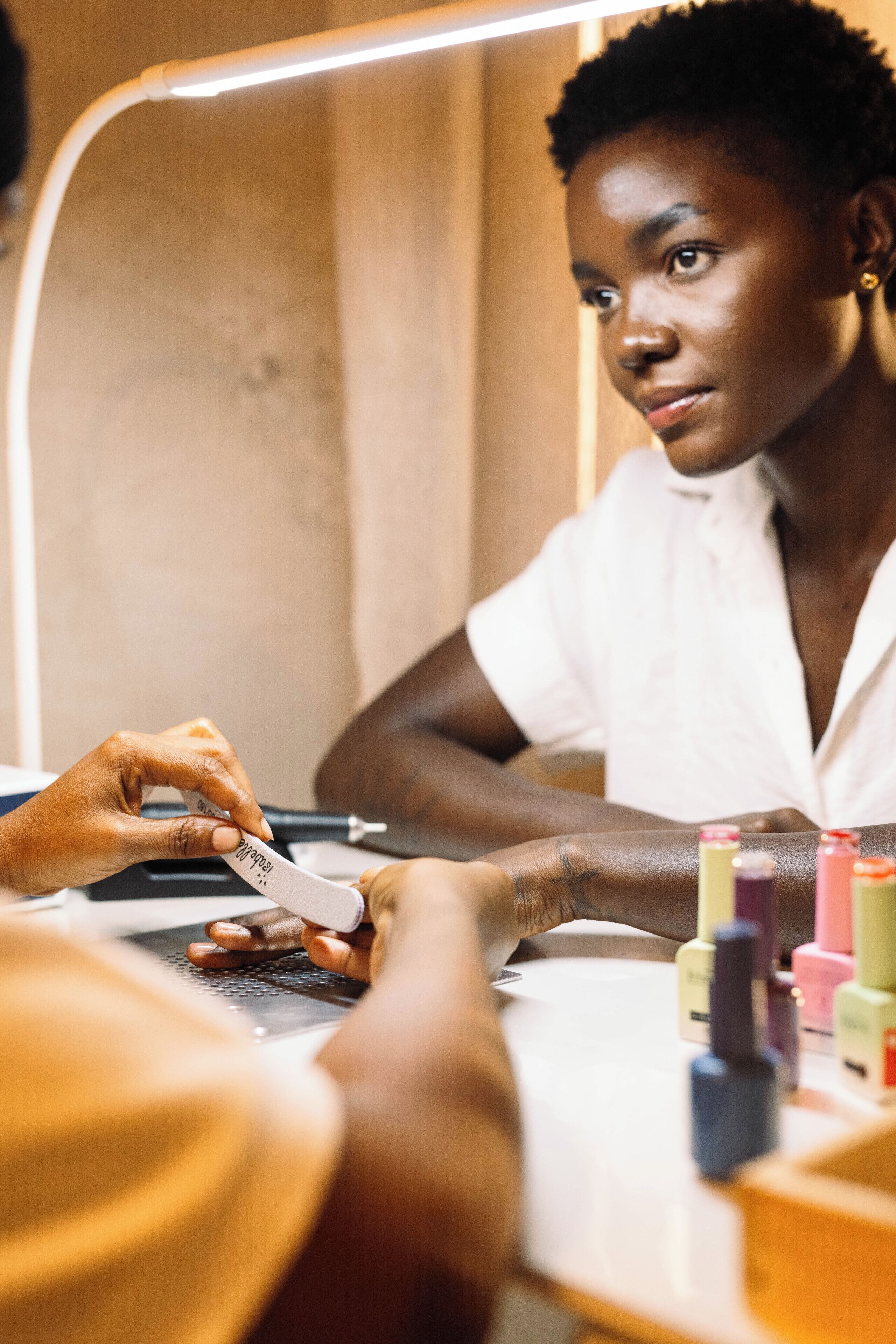 A person sitting at a table with a laptop and nail polish bottles.