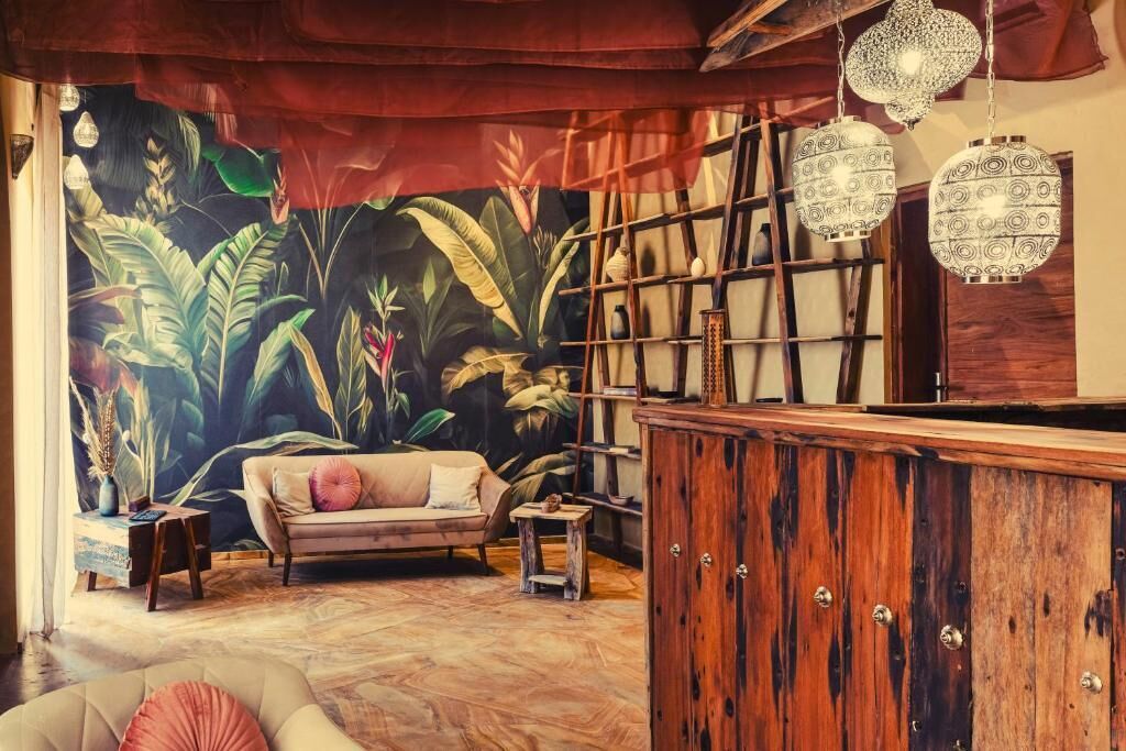A room with a tropical mural, a wooden cabinet, a sofa, and hanging lanterns.