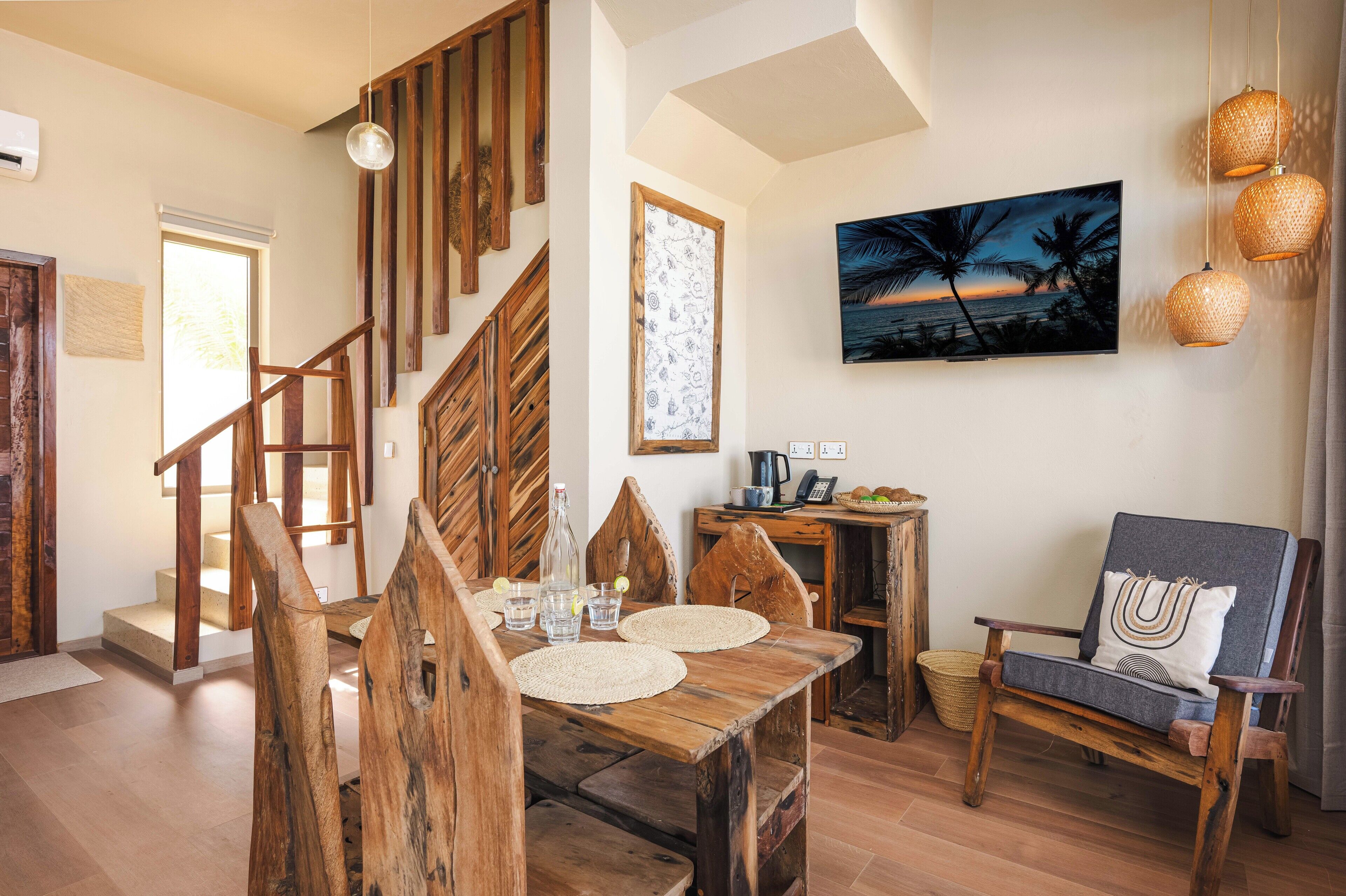 Eine Holztreppe führt zu einem Essbereich mit einem Tisch für zwei Personen, einem Stuhl und einem an der Wand befestigten Fernseher.