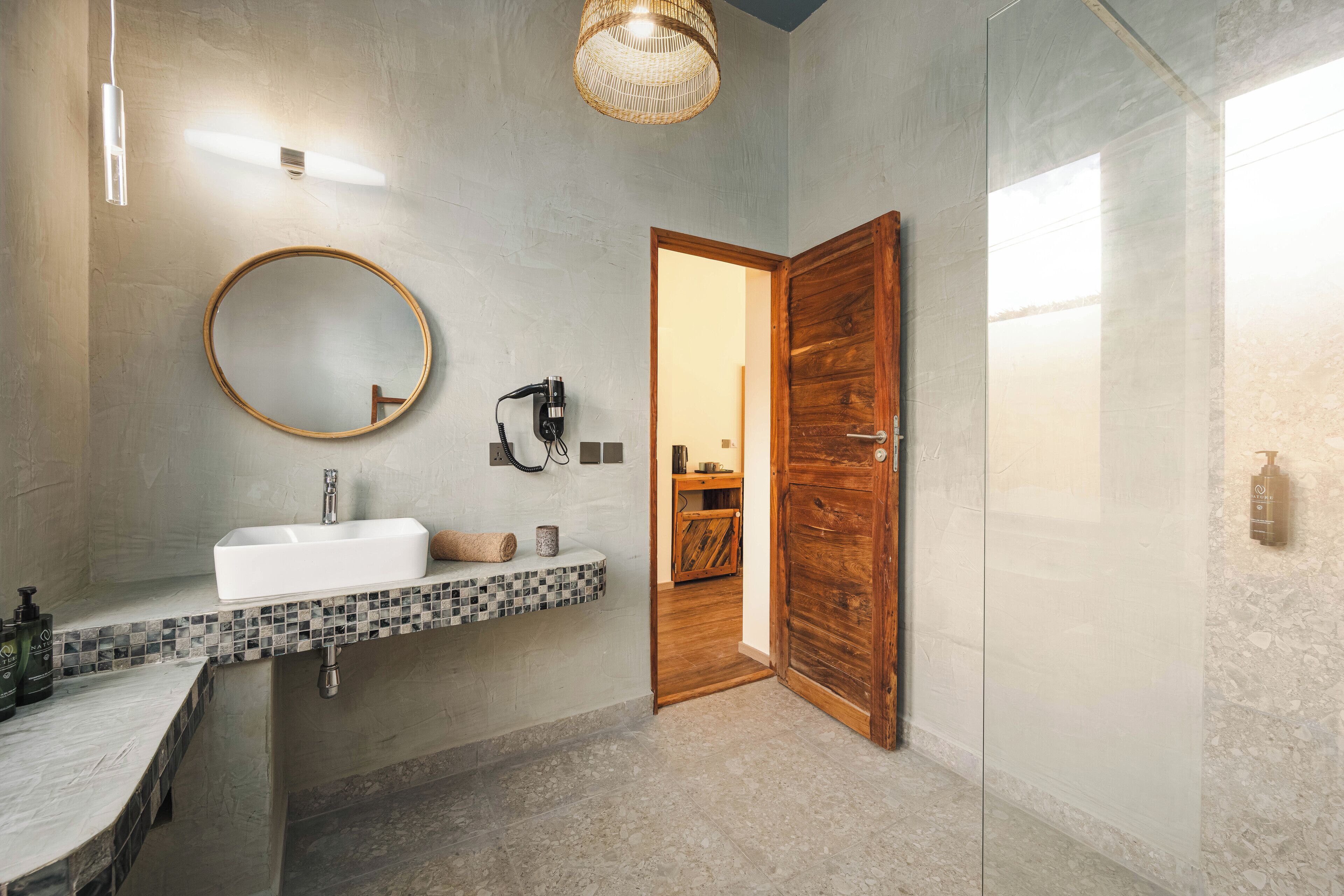 A bathroom with a white sink, a round mirror, and a wooden door.