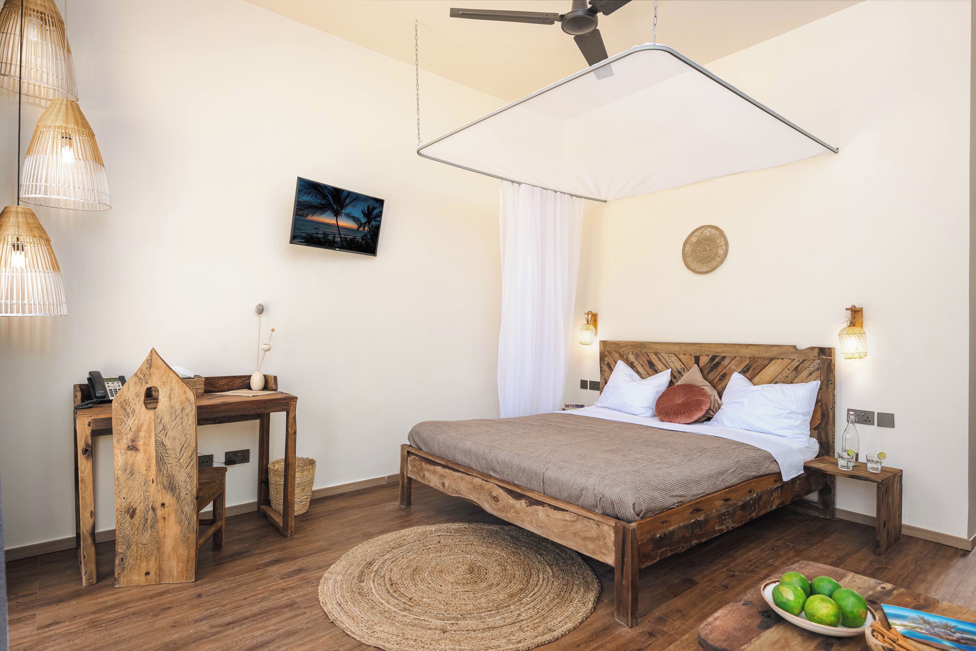 A bedroom with a wooden bed, a desk, a chair, a round woven rug, and a wall-mounted ceiling fan.