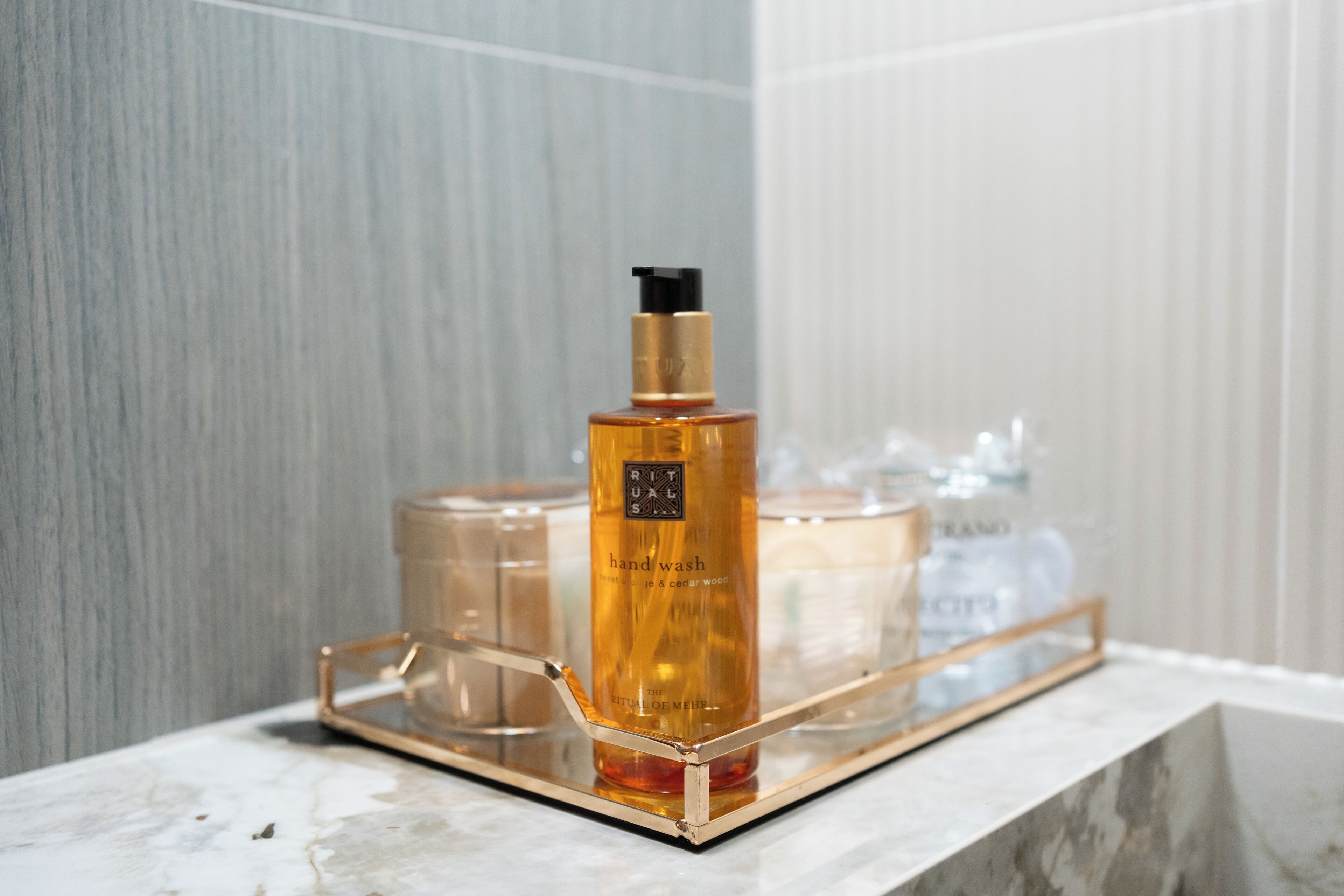 A bathroom with a marble countertop, a gold-framed mirror, and a bottle of hand wash soap.