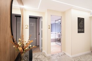 Una hall d'albergo dal design moderno, con un grande specchio, un vaso con fiori secchi e una targa con i numeri delle camere.
