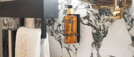 Un baño con pared de mármol, grifo dorado, toallero negro y una botella de jabón de manos.