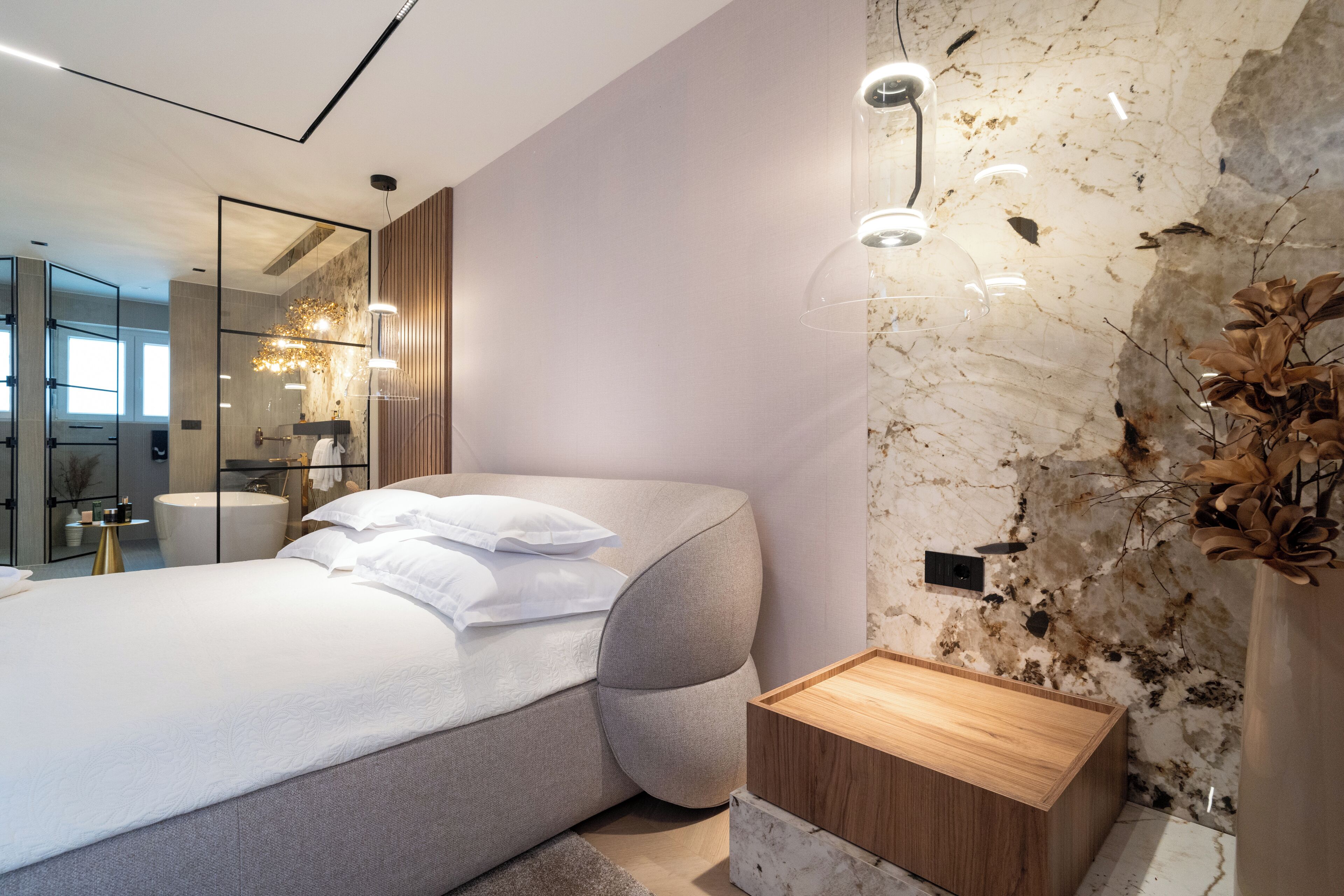 Une chambre à coucher moderne avec un lit aux lignes courbes, une table de chevet en bois et un mur en marbre.