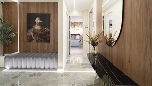 Un vestíbulo moderno con piso de mármol, un banco tapizado en gris, un espejo grande y un cuadro en la pared.