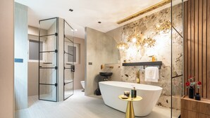 Un baño moderno con una bañera independiente, cabina de ducha con mampara de vidrio y una pared de acento en mármol.