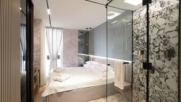 A modern bedroom with a glass shower enclosure, a bed with white linens, and a marble-patterned wall.
