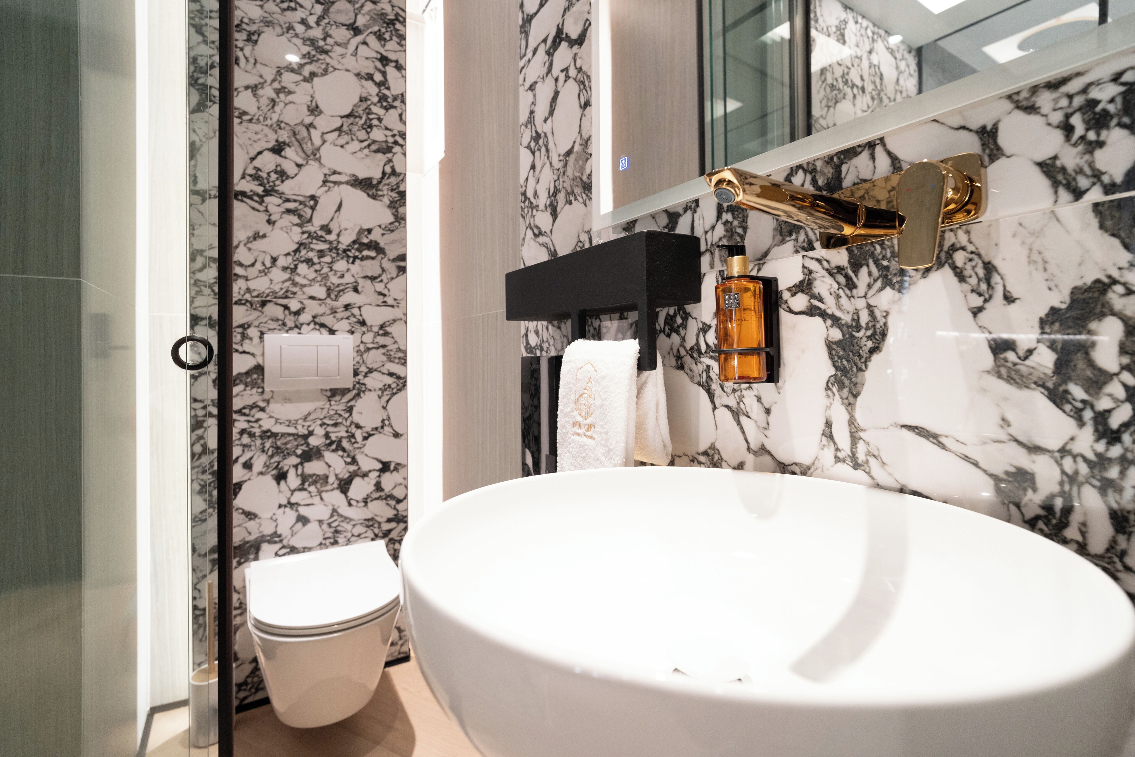 A bathroom with a large white sink, a gold faucet, and a marble backsplash.