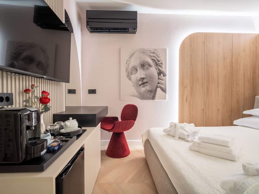 Una habitación de hotel moderna con una cama, una silla roja, una máquina de café y aire acondicionado de pared.
