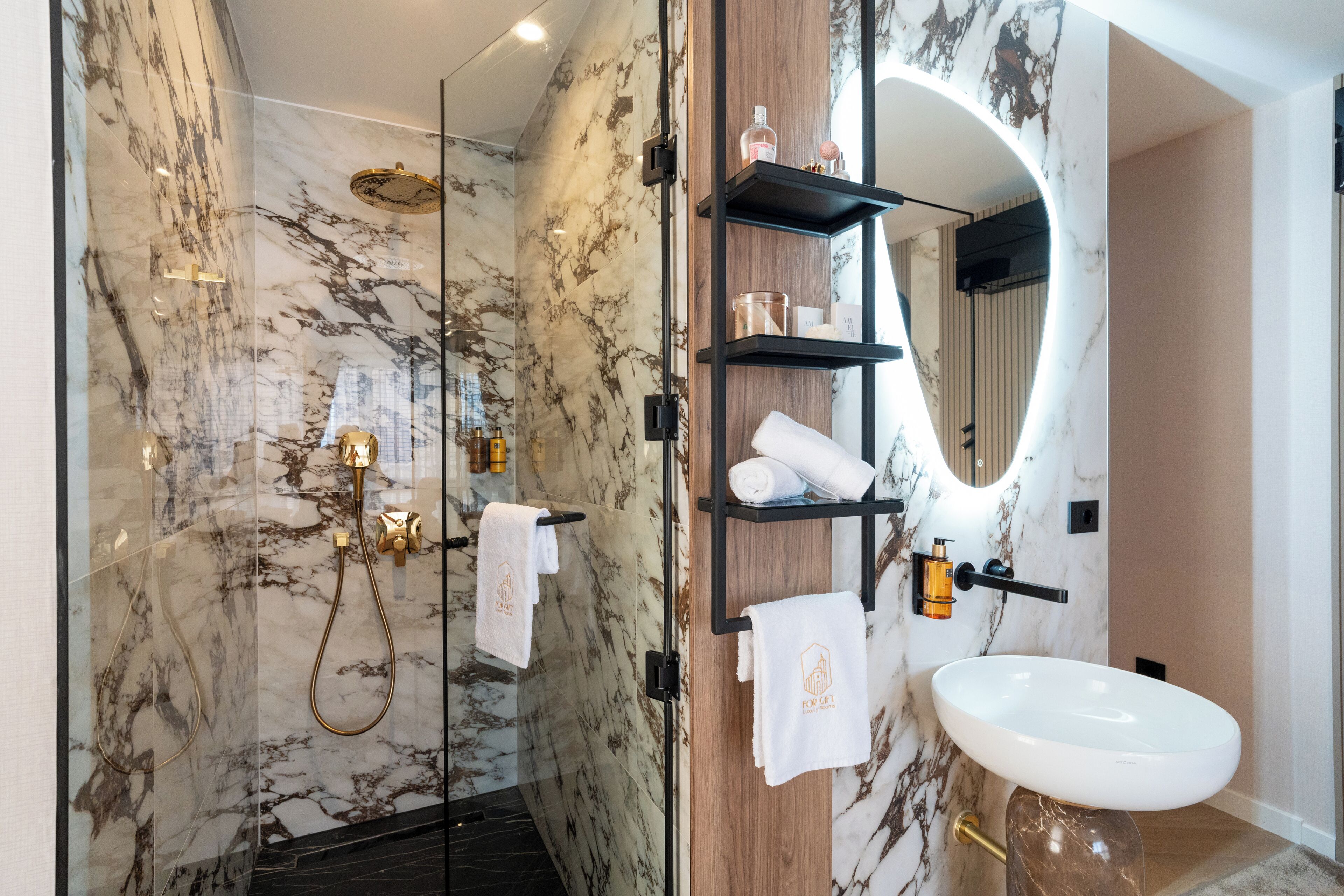 A modern bathroom with a glass-enclosed shower, marble walls, a wooden vanity with shelves, and a white sink.