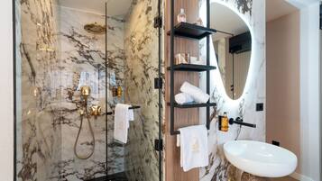 Ein modernes Badezimmer mit einer Duschkabine aus Glas, Marmorwänden, einem Holzbadezimmer-Möbel mit Regalen und einem weißen Waschbecken.