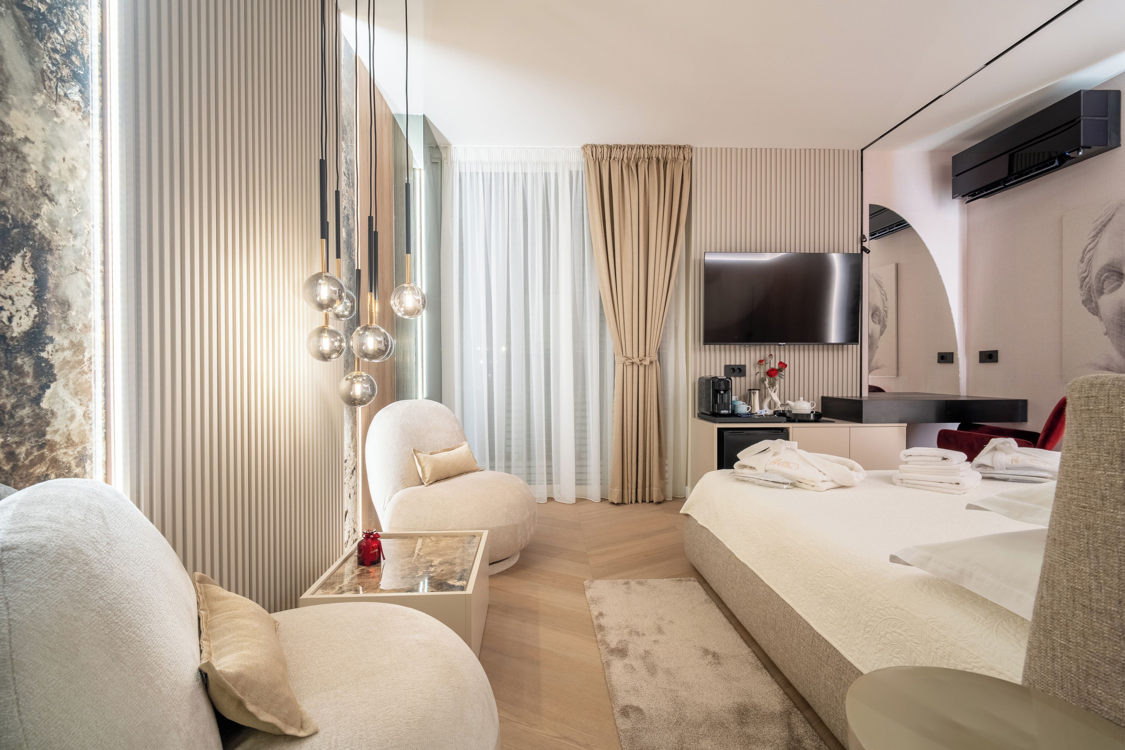 Une chambre d’hôtel moderne dotée d’un grand lit, d’un coin salon avec un fauteuil, d’une petite table avec un vase et d’un téléviseur à écran plat fixé au mur.