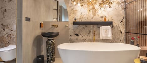 Un baño moderno con una bañera independiente, un tocador de mármol y un espejo montado en la pared.