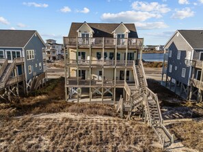 A multi-story beachfront house with a wooden deck and stairs leading to the balconies.