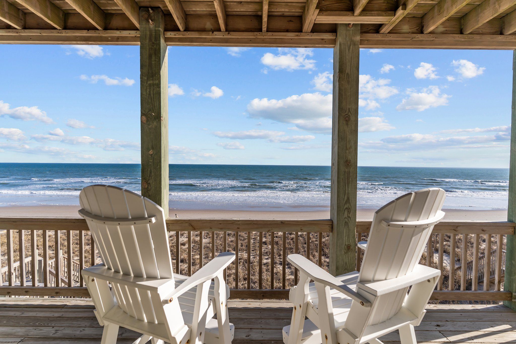 Une terrasse en bois avec deux chaises Adirondack blanches, donnant sur une plage.