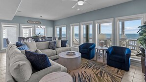 A spacious living room with a large sofa, two armchairs, a coffee table, and a view of the ocean.