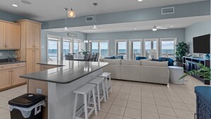 A modern kitchen with a large island, bar stools, and a view of the ocean.