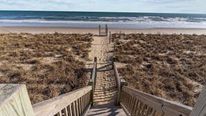 A wooden staircase leading to a beach with a sandy path and grassy dunes.
