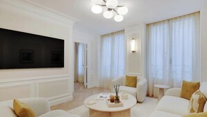 Un salon moderne avec un téléviseur à écran plat, des canapés blancs, une table basse et un lustre.