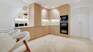 Une cuisine moderne avec des meubles en bois, un four encastré et un coin repas blanc avec une chaise.