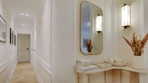 Un couloir doté d’un plancher en bois, de murs blancs et d’une coiffeuse aux lignes courbes, agrémentée d’un miroir, de livres et d’objets décoratifs.