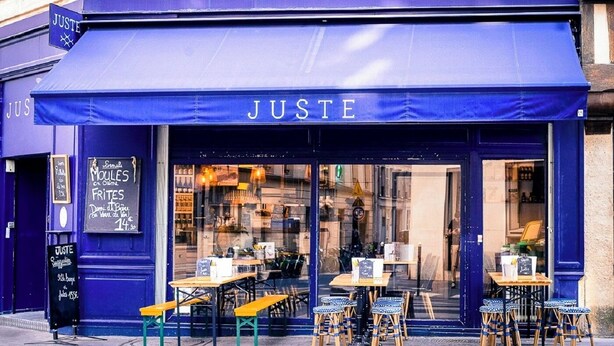 Une devanture bleue portant l’inscription « JUSTE », avec une terrasse aménagée avec des tables et des chaises.