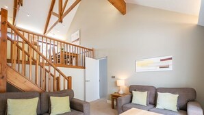 A living room with a staircase, two sofas with cushions, a coffee table with a book, and a lamp on a side table.