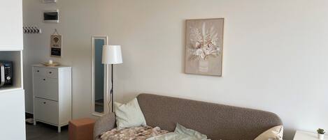 A modern living room with a sofa, a lamp, a framed artwork, and a small table with a plant.