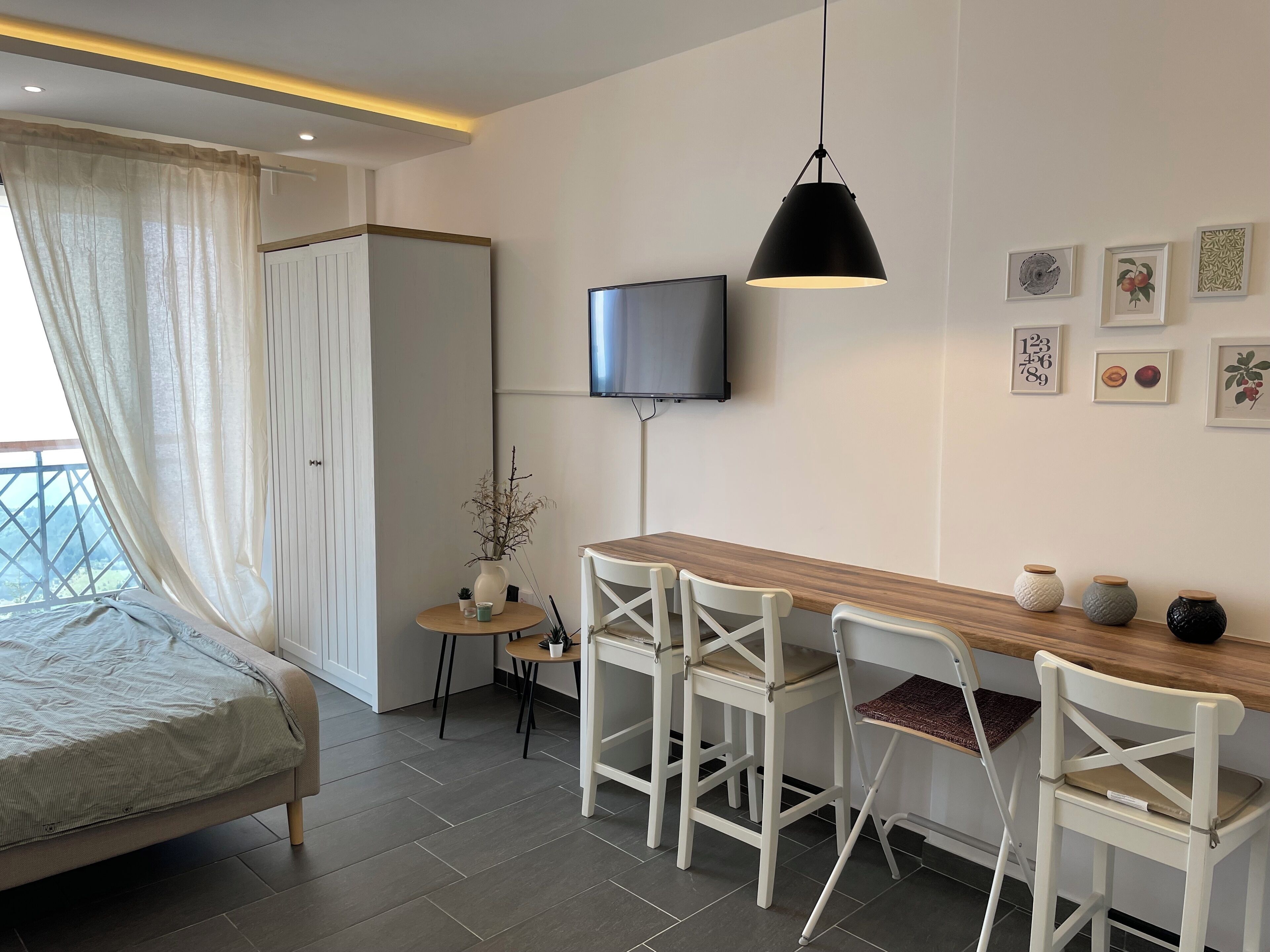 A modern room with a bed, a desk with chairs, a TV, and artwork on the wall.