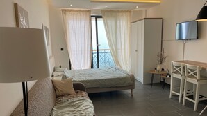 A modern bedroom with a bed, a sofa, a desk with chairs, a TV, and a balcony with curtains. - Residence Hills Lux Hotels & Spa Kopaonik (Raška)