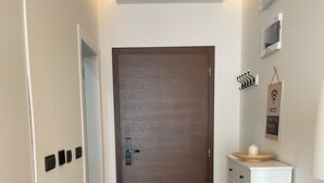 A narrow hallway with a wooden door, a white cabinet with drawers, a small round table with a candle, and a wall-mounted WiFi sign. - Residence Hills Lux Hotels & Spa Kopaonik (Raška)