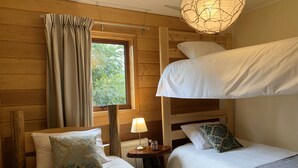 A room with two beds, a window with curtains, a lamp, and a hanging light fixture. - Cumbres de Chiloé (Castro)