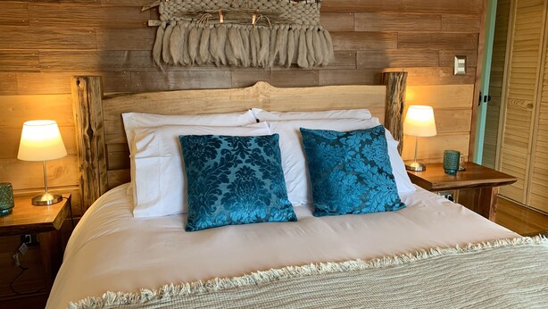 A bed with white linens, two blue patterned pillows, and a woven throw blanket. - Cumbres de Chiloé (Castro)