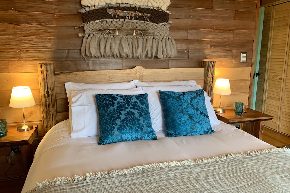Ein Bett mit weißer Bettwäsche, zwei blau gemusterten Kissen und einer gewobenen Tagesdecke.