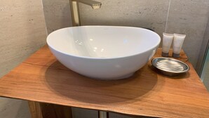 A bathroom with a large white vessel sink, a gold faucet, and two toiletry tubes on a wooden vanity. - Cumbres de Chiloé (Castro)