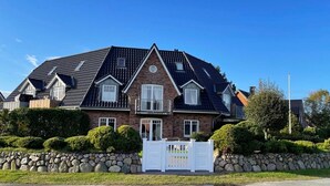 A large, two-story house with a steeply pitched roof, a stone foundation, and a white gate in the front. - Comfortable, fully equipped vacation apartment with terrace and garden access (List)