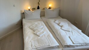 A double bed with white linens and towels, two bedside tables with lamps, and a small vase with flowers on one table. - Comfortable, fully equipped vacation apartment with terrace and garden access (List)