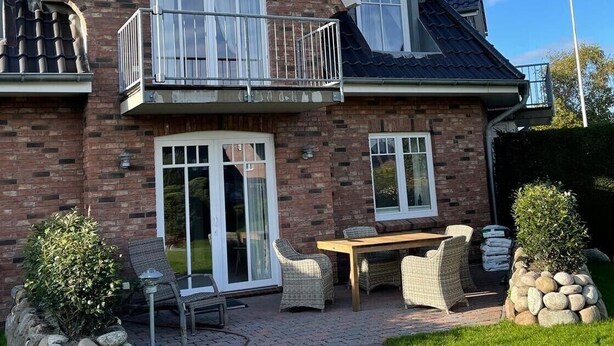 A two-story house with a brick facade, a balcony, and a patio area with outdoor furniture. - Comfortable, fully equipped vacation apartment with terrace and garden access (List)