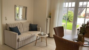 A living room with a striped sofa, a round coffee table, wicker chairs, a large mirror, and a view of a garden through a sliding glass door. - Comfortable, fully equipped vacation apartment with terrace and garden access (List)