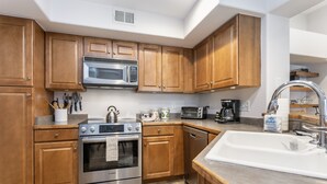 A modern kitchen with wooden cabinets, stainless steel appliances, and a white sink. - River Pines A303 3 Bedroom Condo (Edwards)