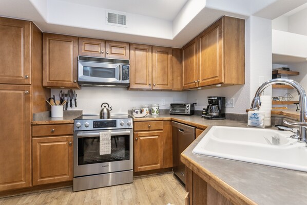A modern kitchen with wooden cabinets, stainless steel appliances, and a white sink. - River Pines A303 3 Bedroom Condo (Edwards)