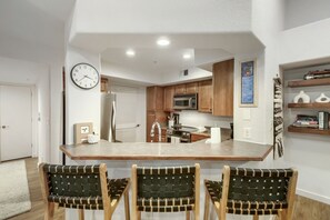 Una cocina moderna con una isla central, armarios de madera, un refrigerador de acero inoxidable y un reloj en la pared.